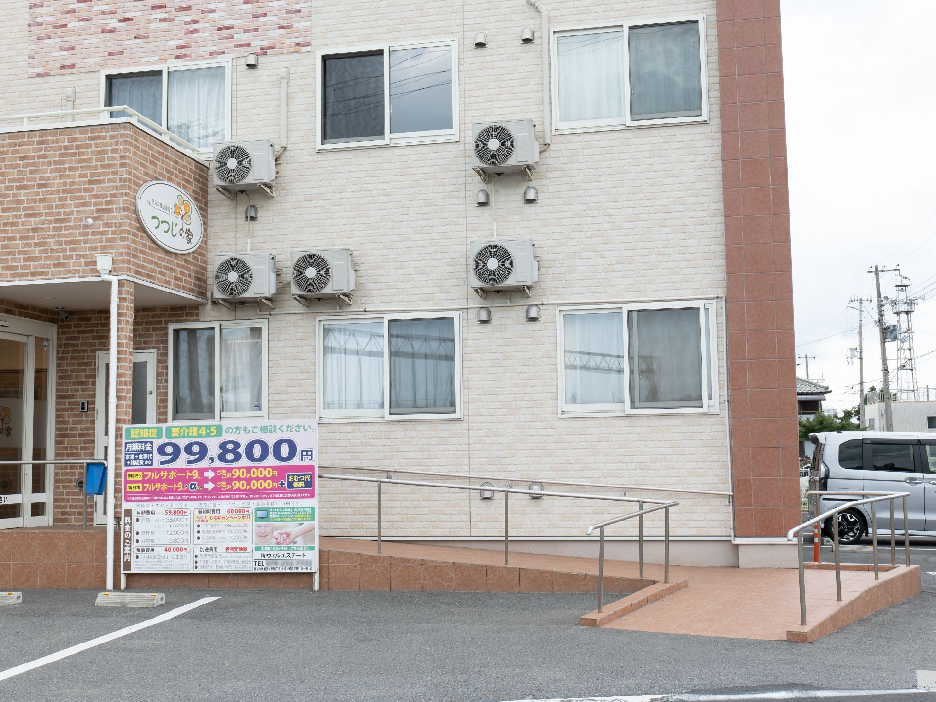 手すり付きのスロープがあり、駐車場も付いている2階建ての建物はベージュ系でまとめられている。
