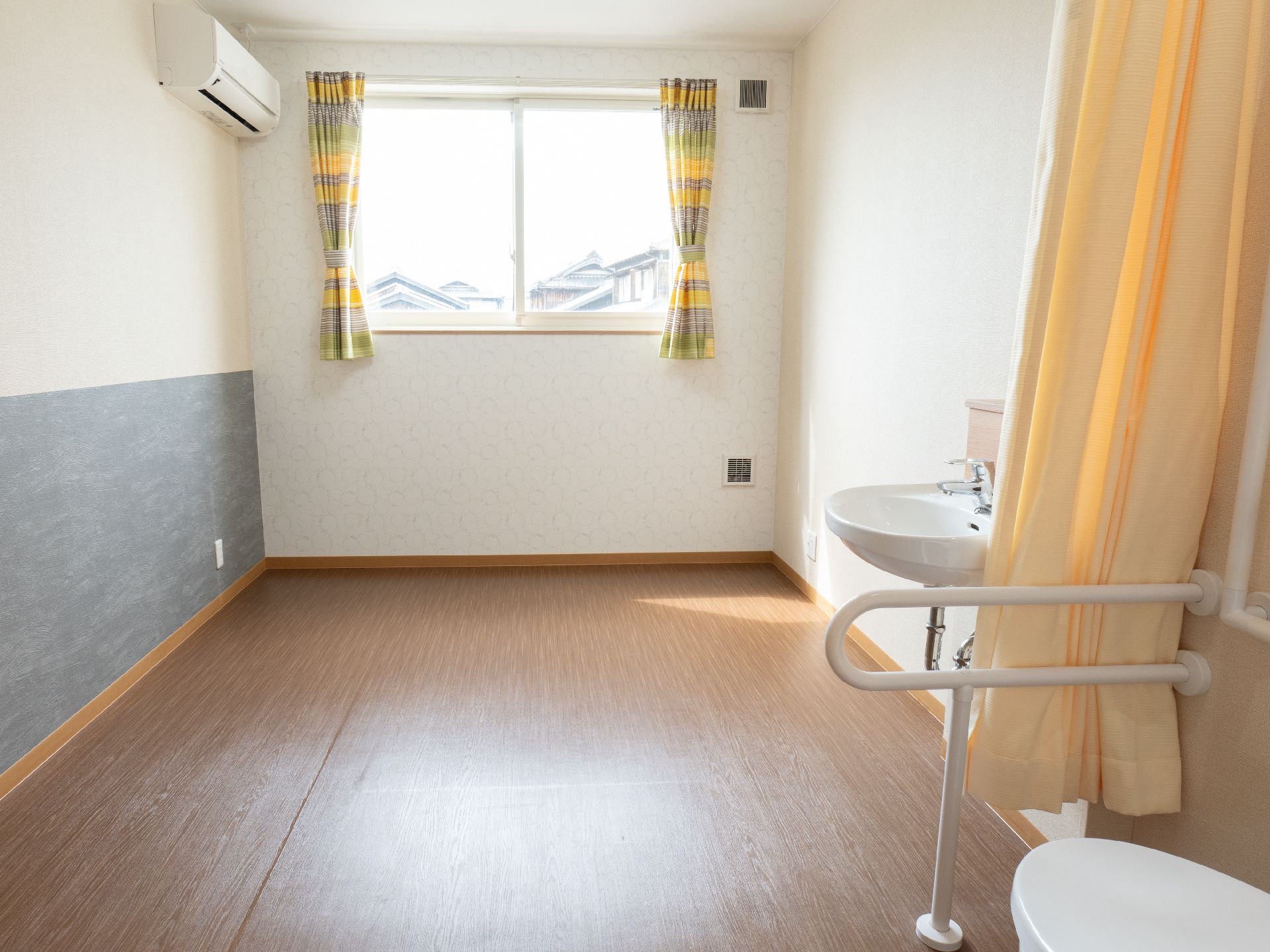 壁沿いにトイレと洗面台がある大きな窓がついた部屋