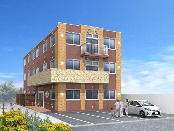 3階建ての建物はブラウン系で住宅名が壁に書かれている。駐車場には車が止まり、家族連れがいる。