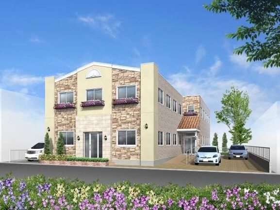 2階建ての建物の玄関には手すり付きのスロープと屋根があり、敷地内には駐車場があり、車が止まっている。