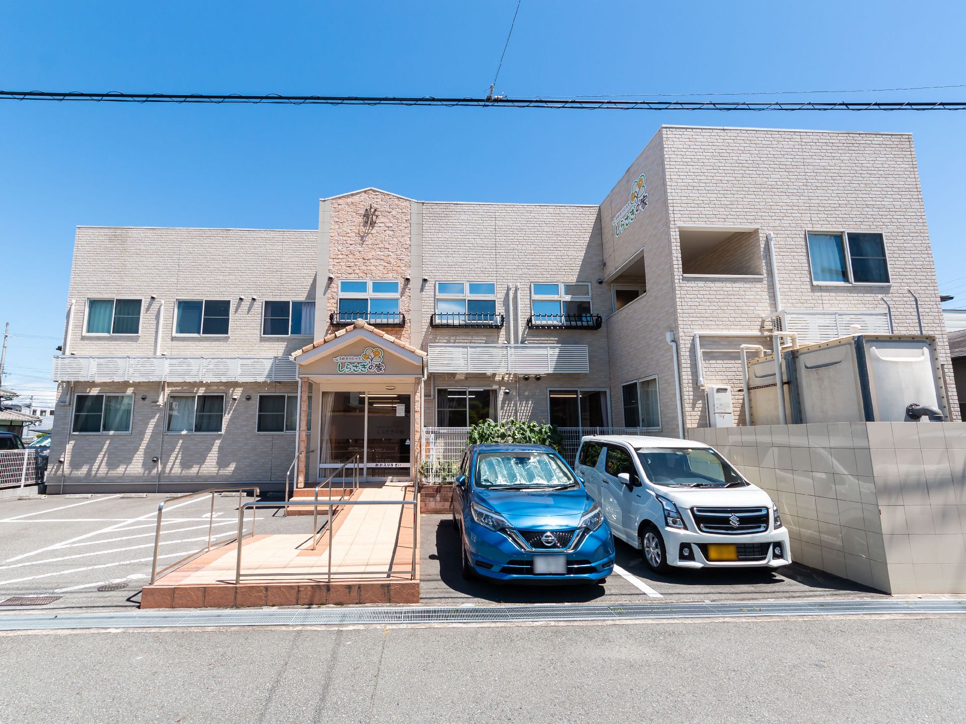 目の前に車が２台止まった駐車場があるベージュ系の外観で２階建ての建物