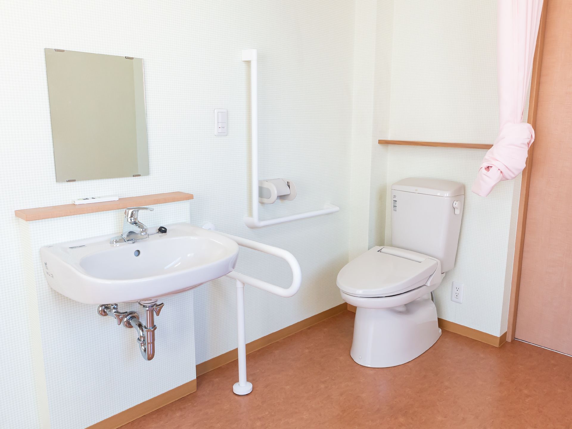 白い壁際に配置された洗面台と白い手すりに囲まれた洋式便器