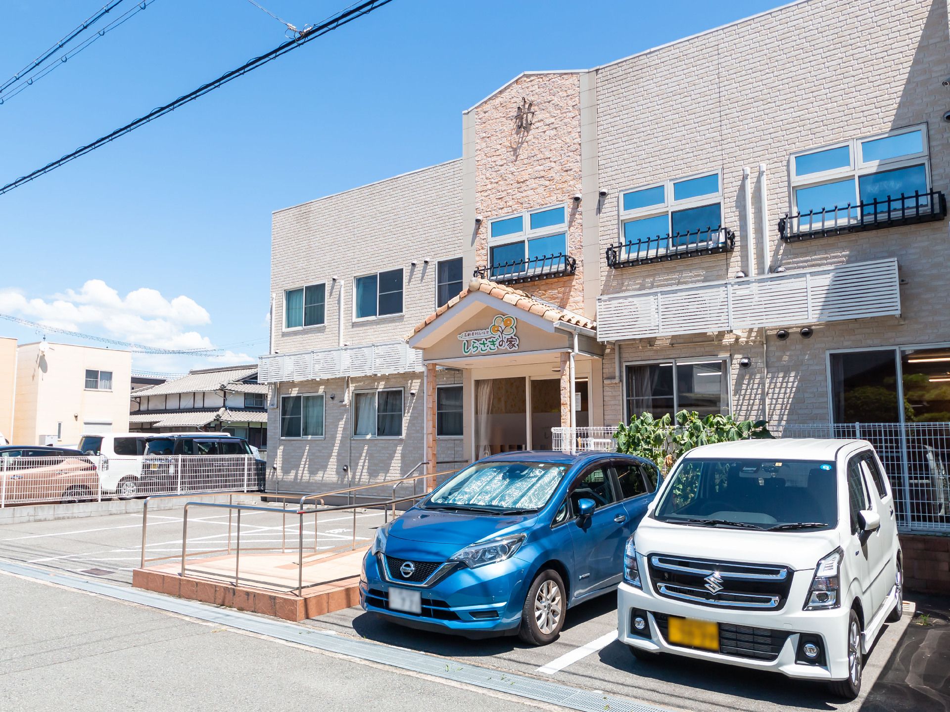 車が２台止まった駐車場が目の前にあるベージュ系の外観で２階建ての建物