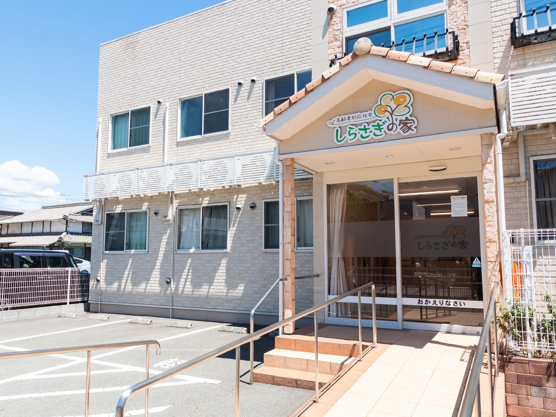ベージュ系の外観で２階建ての建物の入り口にある手すり付きのスロープ