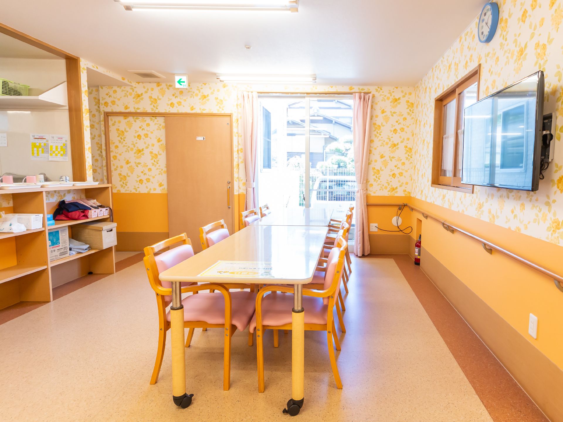 木製の机と椅子が置かれた手すりが付いた花柄の壁の広間