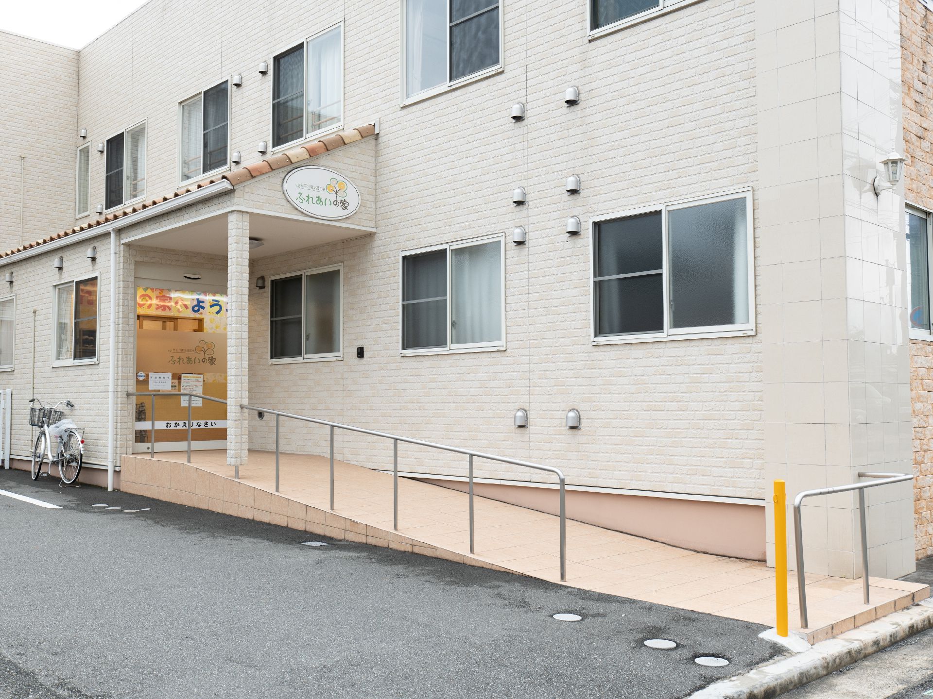 ピンクのエプロンを付けた若い女性スタッフが笑顔で車いすの高齢女性と散歩をしている。