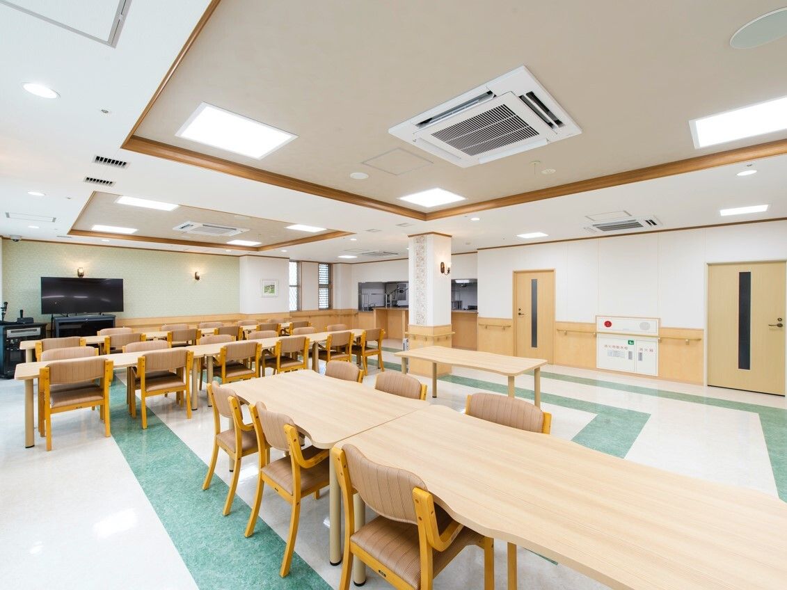 木製のダイニングテーブルセットが複数置かれた食堂にはテレビもあり、椅子がセットされていないところもある。