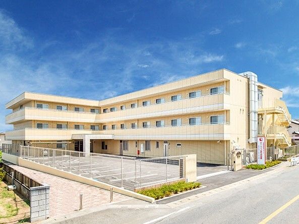広い駐車場がある3階建ての建物はエル字型で各フロアにベランダがあり、日当たりのいい場所に建っている。