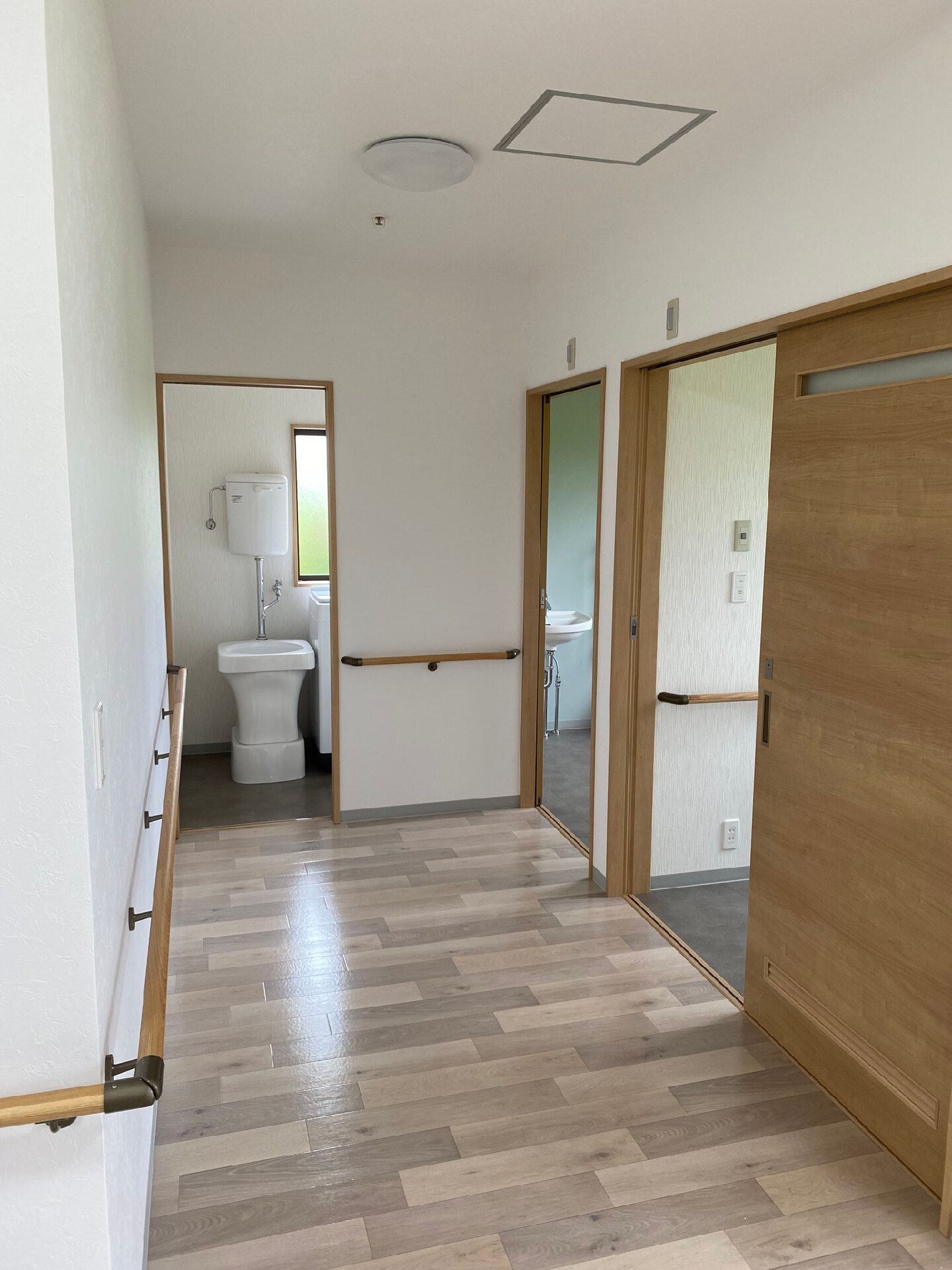 トイレが廊下の突き当りに複数設置されていて、いずれもドアが開いている。廊下には手すりが付いている。
