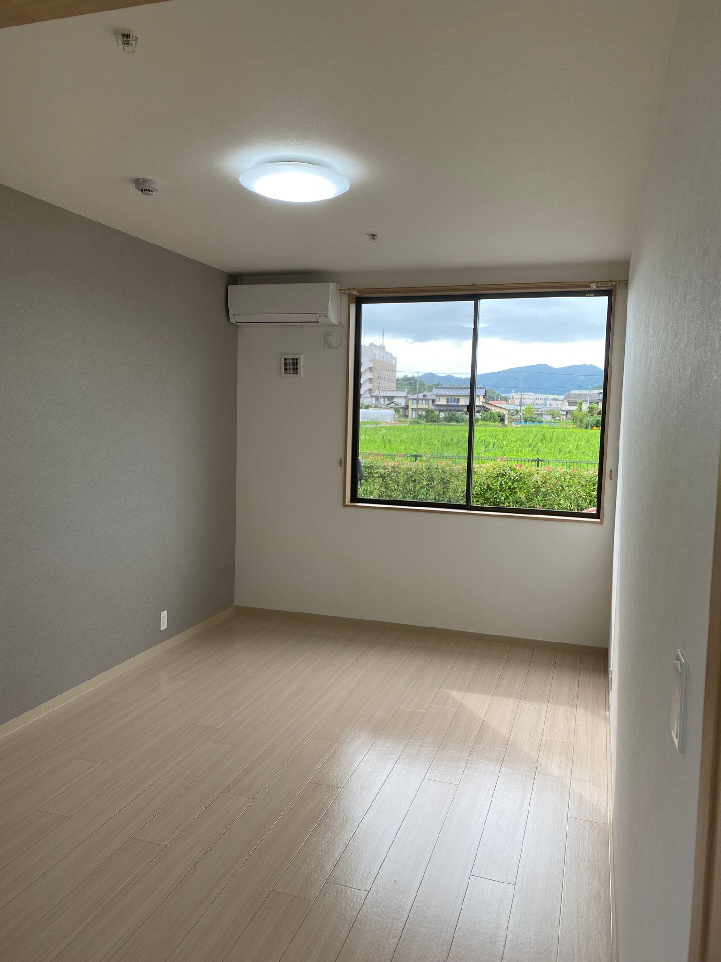 大きな窓の外には田園風景が広がっていて、窓の横にはエアコンがある。居室には家具などはない。