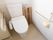 温水洗浄便座器が完備されているトイレである。白い壁には、手すりが設置されペーパーホルダがかかっている。