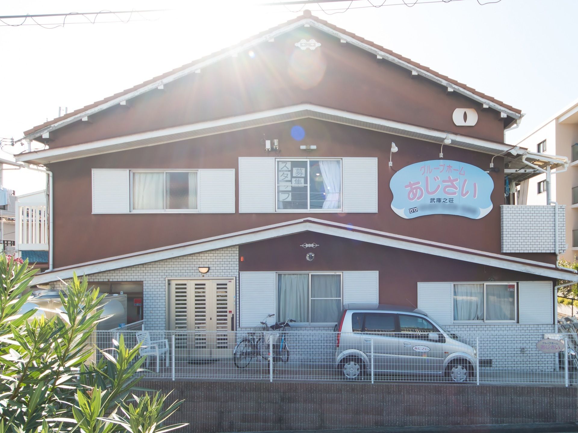 晴天の日に正面から見た2階建て施設の様子である。ブラウン系の外壁面に、施設プレートがある。
