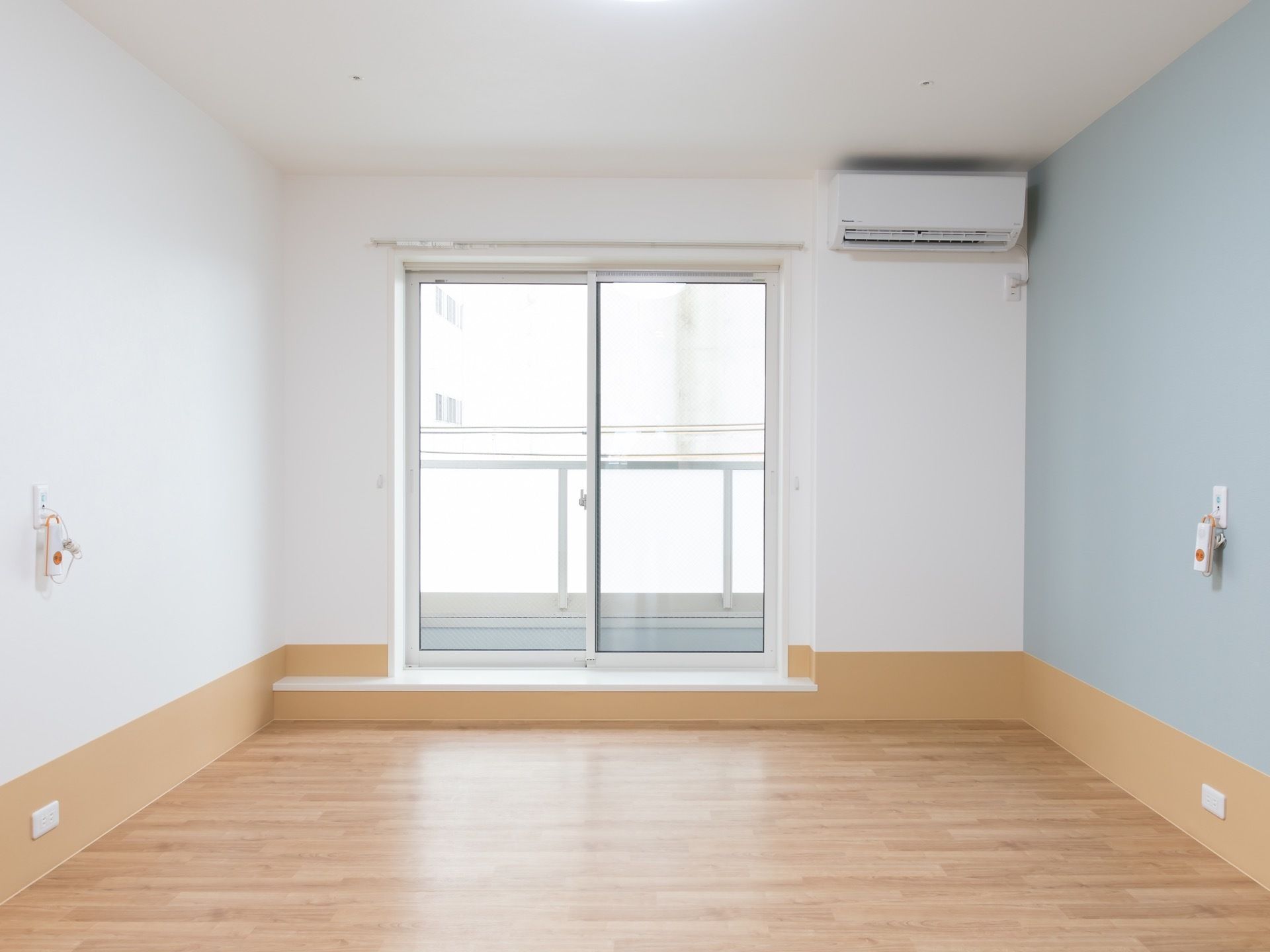 フローリング造りのシンプルな居室である。広々とした、掃き出し窓が備え付けられている。となりにはエアコンがある。