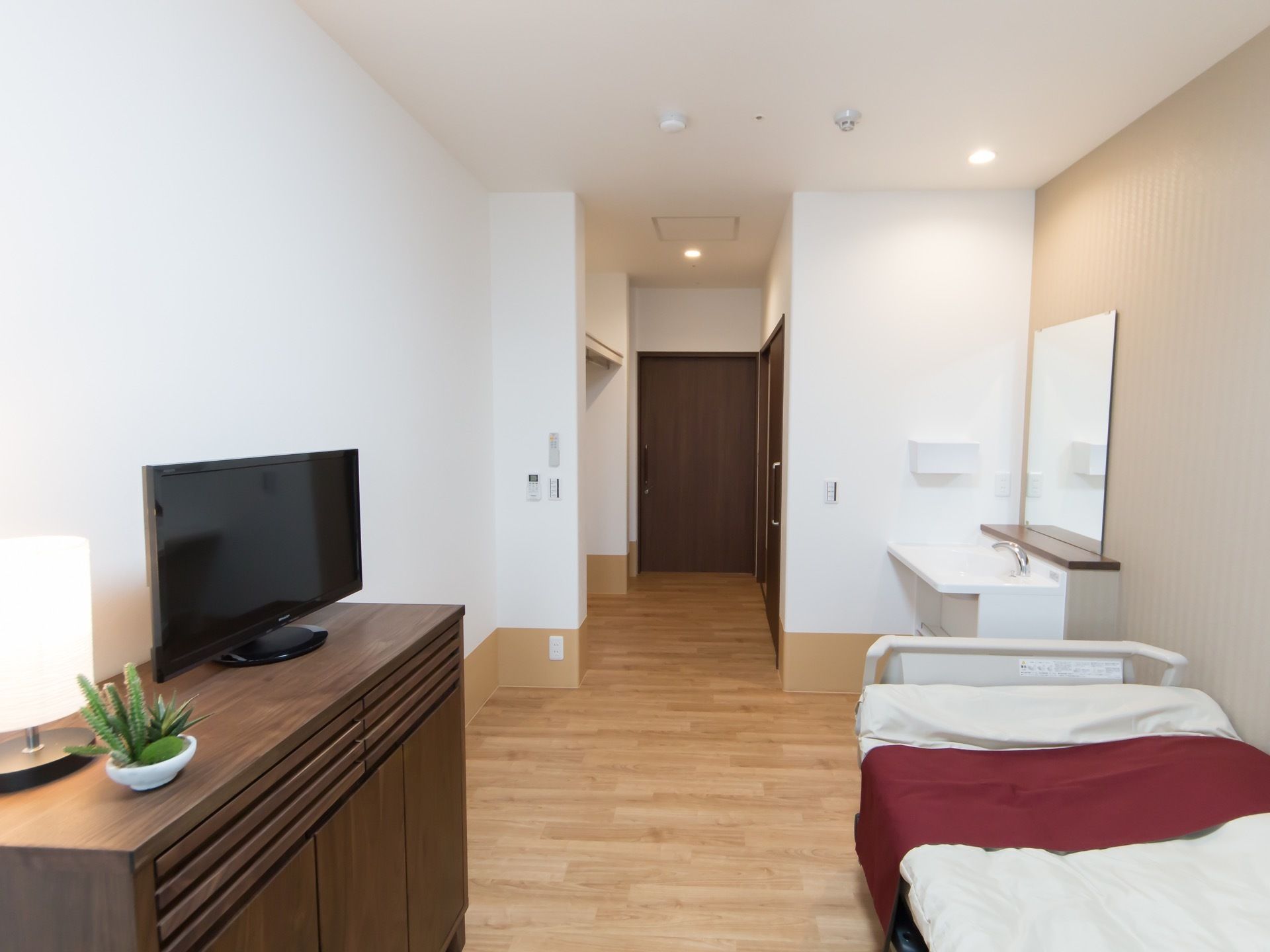 フローリングの洋部屋である。ベッドや鏡付きの洗面台、収納家具が設置されている。小型のテレビも置かれている。