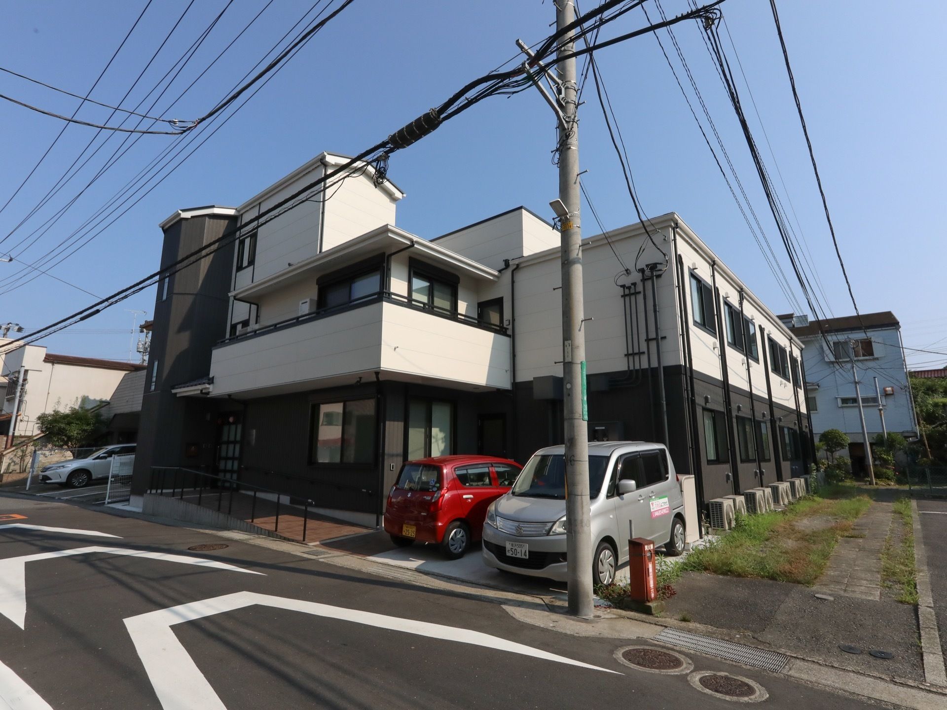 ツートンカラーの外壁が特徴の２階建て施設である。２階部分には、ベランダが設置されている。エントランスのスロープには、手すりが付いている。