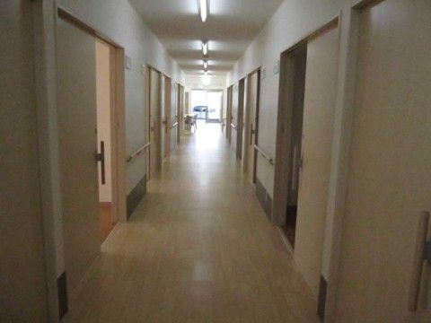 淡い木目調のオシャレな雰囲気の廊下である。光沢のある床は凹凸がなくゆったりしている。左右の壁には手すりがある。
