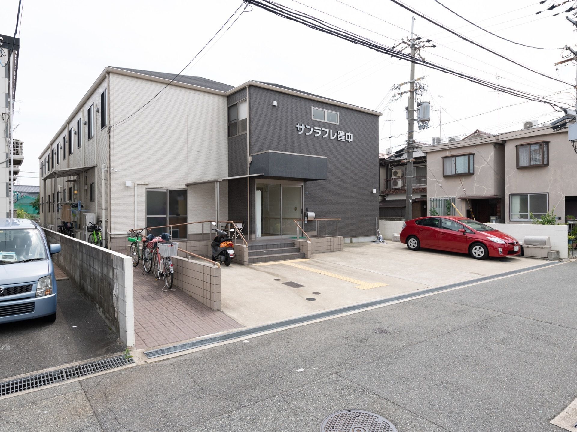 施設は閑静な住宅地に立地している。敷地内に駐車スペースが設けられている。手すり付きのスロープが設置されている。