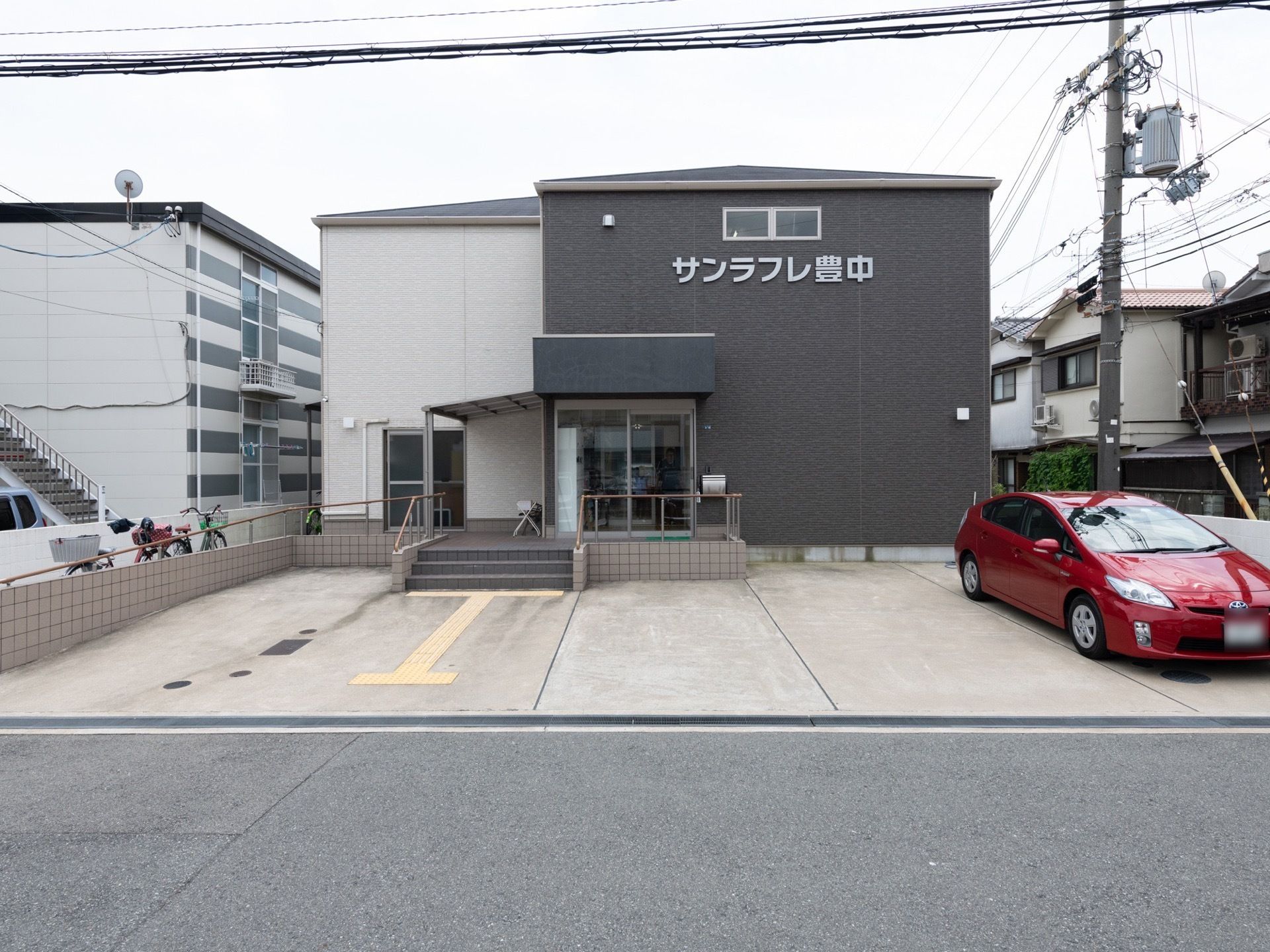 施設の前面に白い大きな文字で施設名が書かれている。玄関までは段差の低い階段があり、手すりが設置されている。