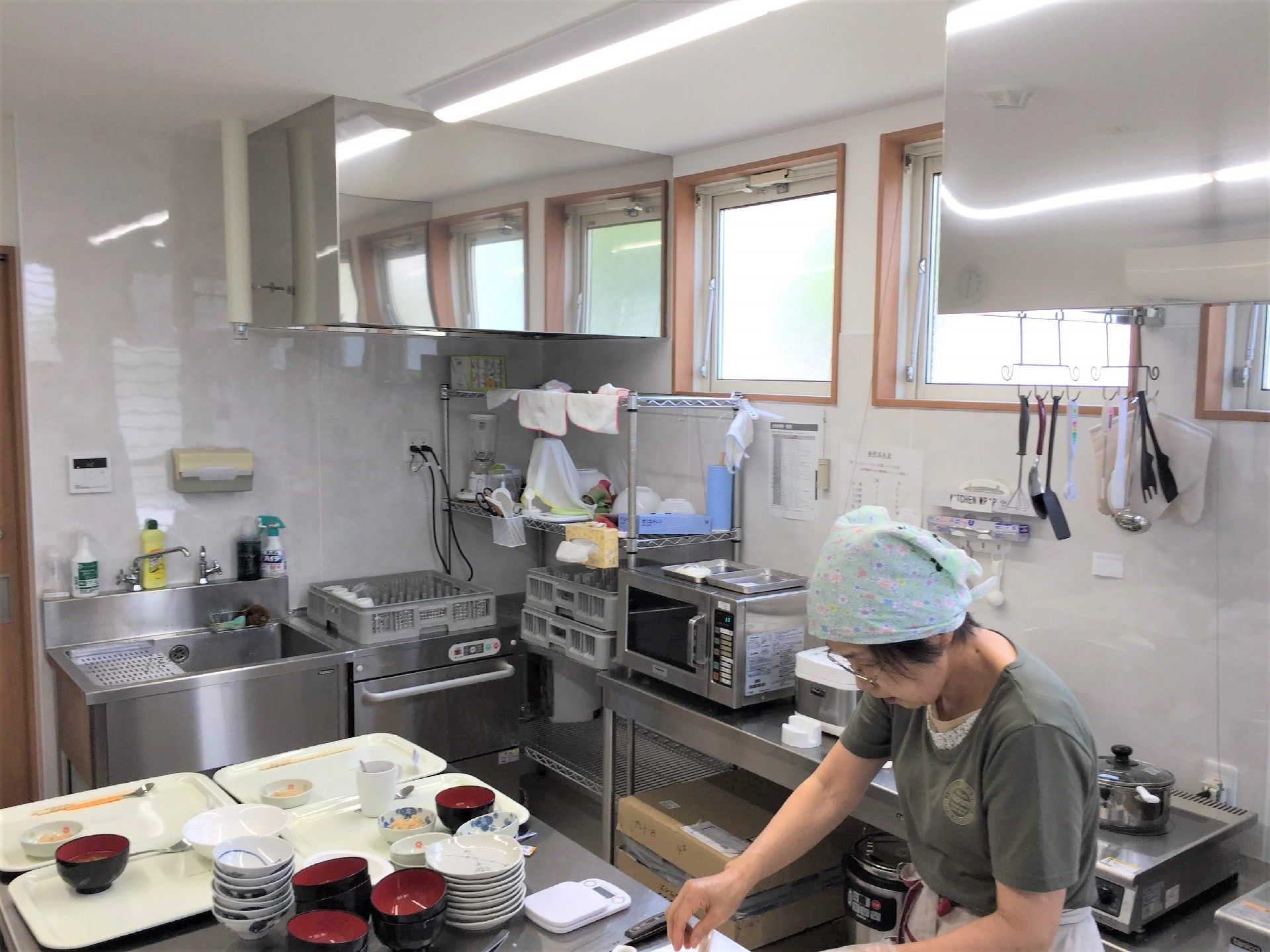 厨房で三角巾をかぶった女性が食事の調理をしている。
