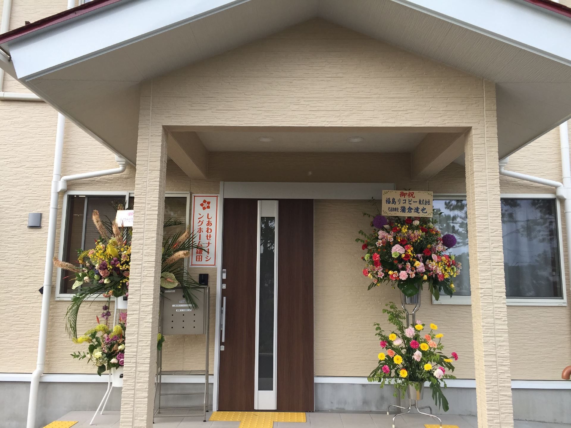 玄関にはたくさんの花が並び、屋根が付いている。ドアの横には表札もある。