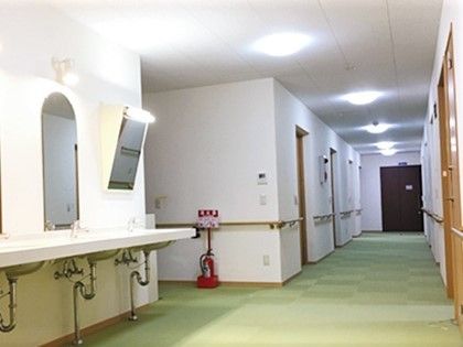 施設内の廊下の様子。左側に洗面台、右側に個室のドアが並ぶ廊下が写っている