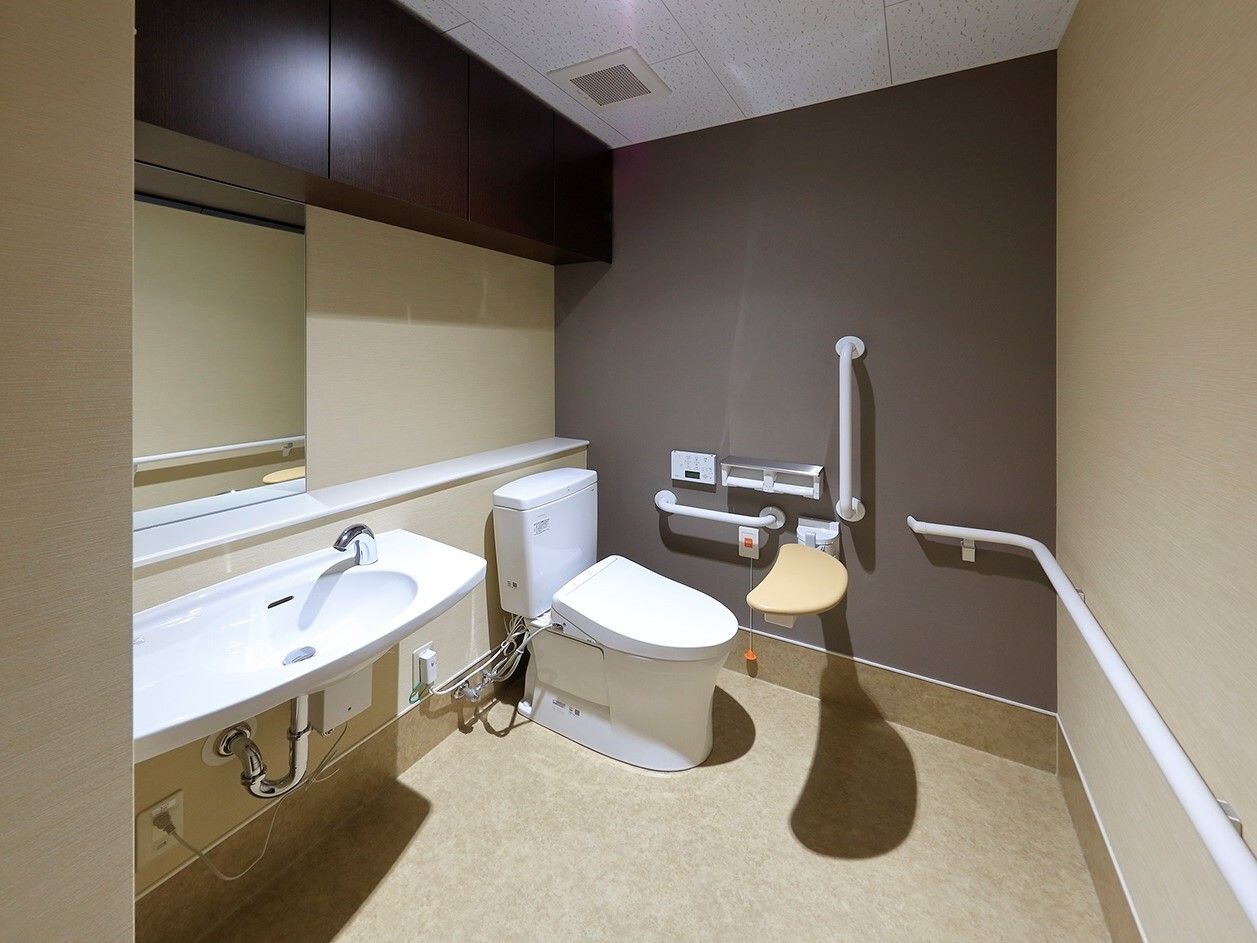 鏡付きの手洗い場が設置されたトイレは広く、壁一面に手すりがあり、便座の前にはバー、横には呼び出しボタンが付いている。