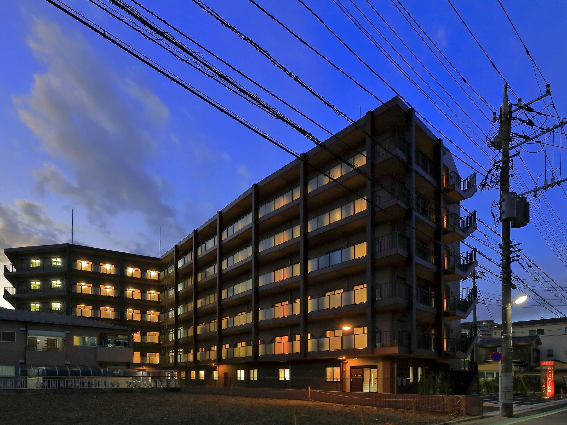 夕暮れ時になりあたりが暗くなっている中、大きな6階建ての建物の内部には明かりが灯っている。