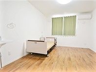 ベッドやエアコン、洗面などが置かれたフローリングの居室。大きな窓にはカーテンもある。