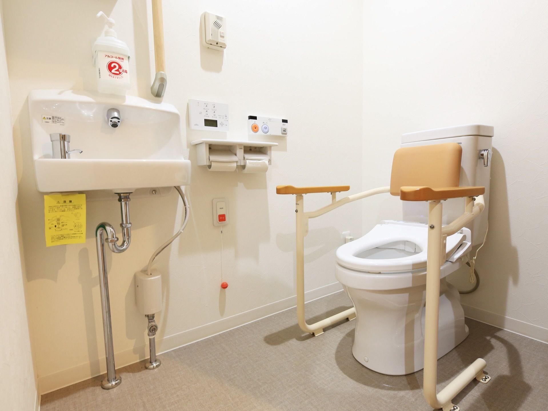 便器の両脇に手すりが設置されており、壁にはナースコールやペーパーホルダー、トイレ用のリモコンが取り付けられている。