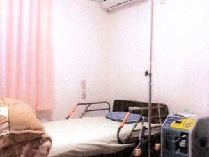 電動ベッドのある居室。白い壁や天井があり、窓にはピンクのカーテンが引かれている