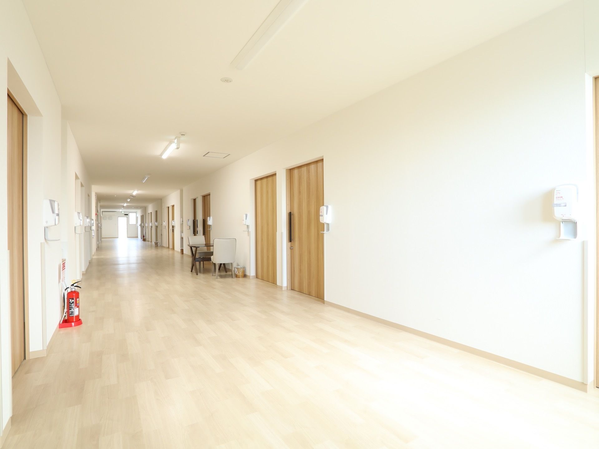 通路はとても広々としており、白い内装の明るい空間である。左側の壁際には消火器が置かれていて、右側にはテーブルと椅子が設置されている。