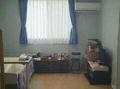 フローリングの部屋には大きな窓があり、カーテンが付いている。ベッドやいすなどの家具も置かれている。