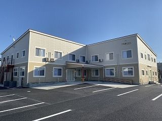 エル字型のベージュ系の建物が広い敷内に建っていて、玄関には大きな屋根が付いている。