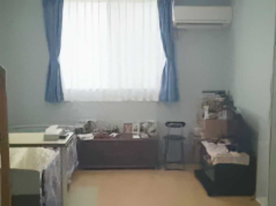 フローリングの部屋には大きな窓があり、カーテンが付いている。ベッドやいすなどの家具も置かれている。