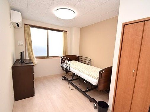 ベッドやテレビが置かれたタンス、エアコンなどがある居室はフローリングで大きな窓が付いている。