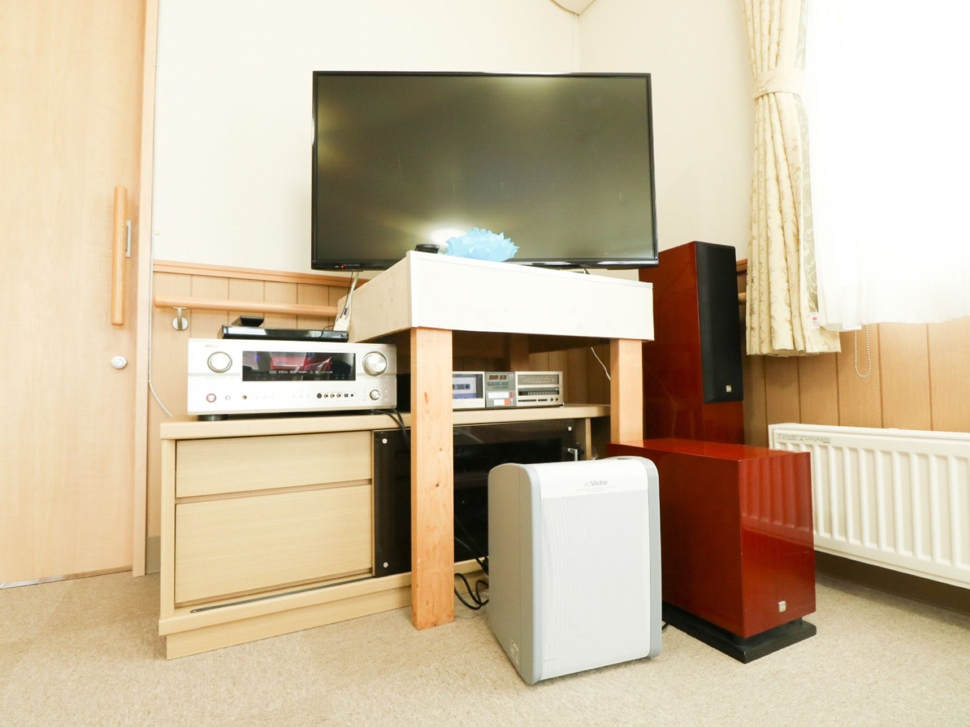 部屋の一角に、テレビやスピーカーなどを集めた音響システムがある。細長く背の高い赤色の器具も置かれている。