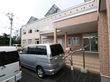 玄関前に大きなひさしがある。ひさしの下でタオルが乾かされている。階段を下りた所に車が停められている。