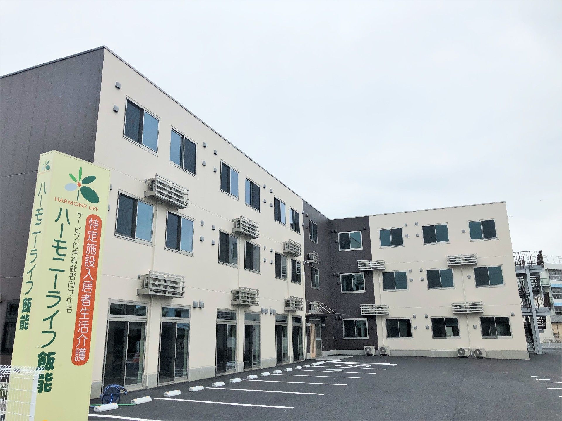 広い駐車場が付いた3階建ての建物。玄関には屋根が付き、屋外階段も付いている。