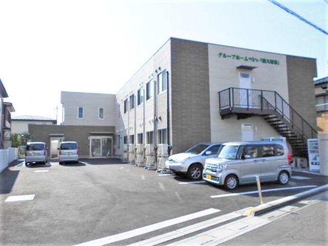 2階建ての建物はグレー系で、屋外階段や駐車場、自動販売機もある。