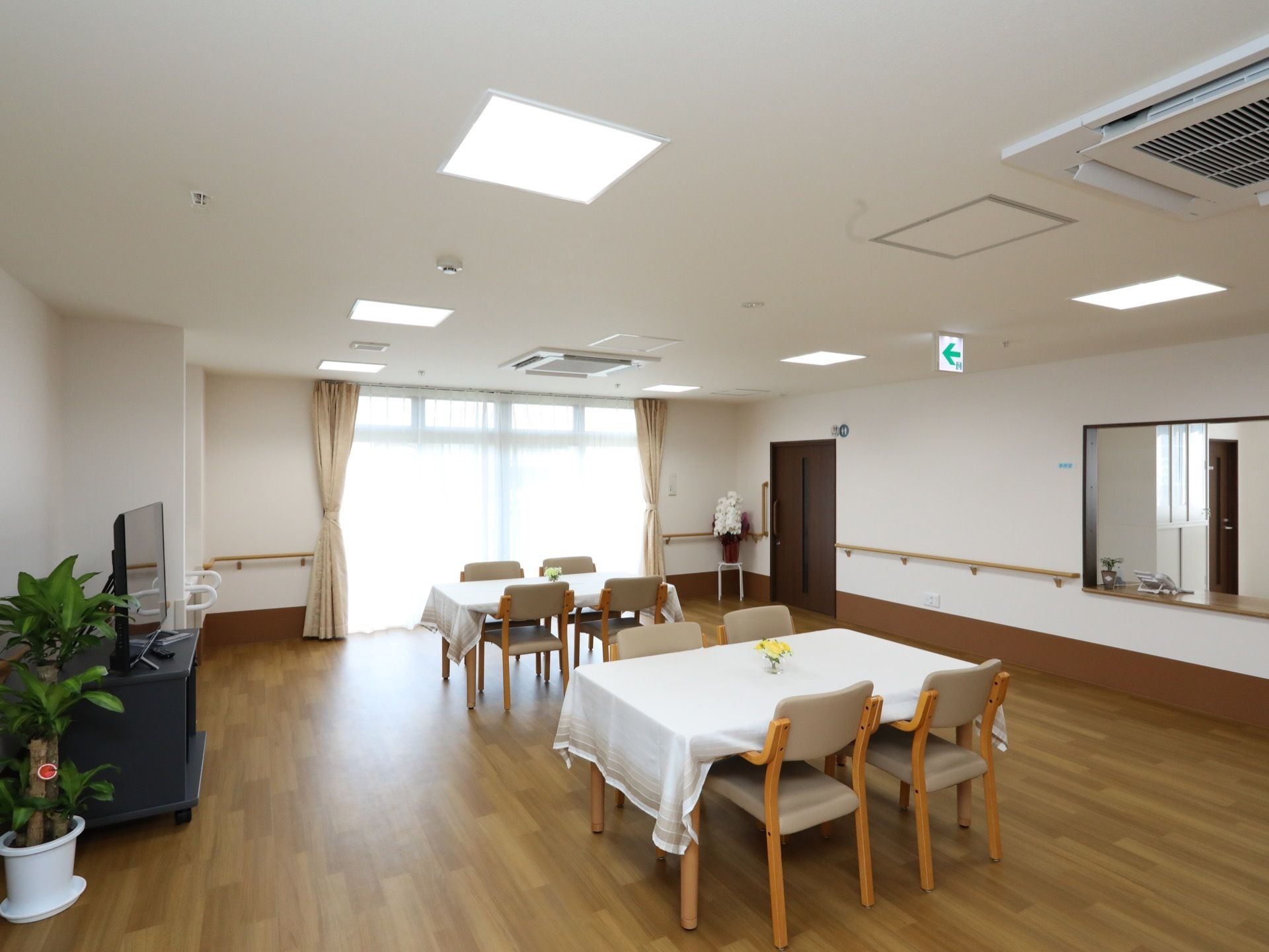 壁には手すりが取りつけられ、中央にテーブルと椅子が並べられている。壁際にはテレビや観葉植物が配置してある。