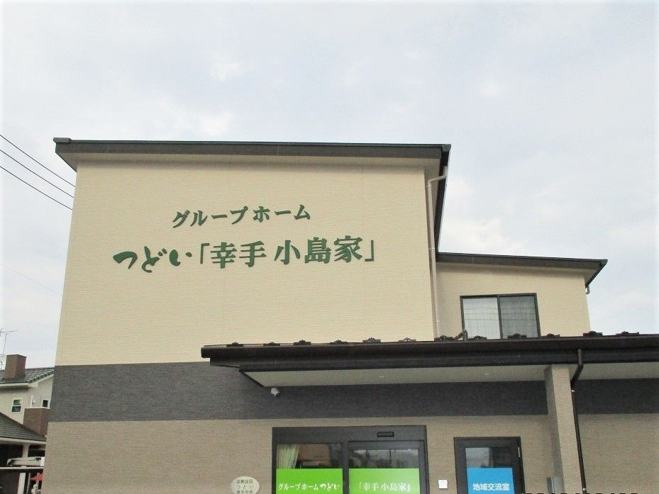 ベージュ系の2階建ての建物。玄関部分には二つの出入り口と屋根が付き、ホーム名が外壁に書かれている。