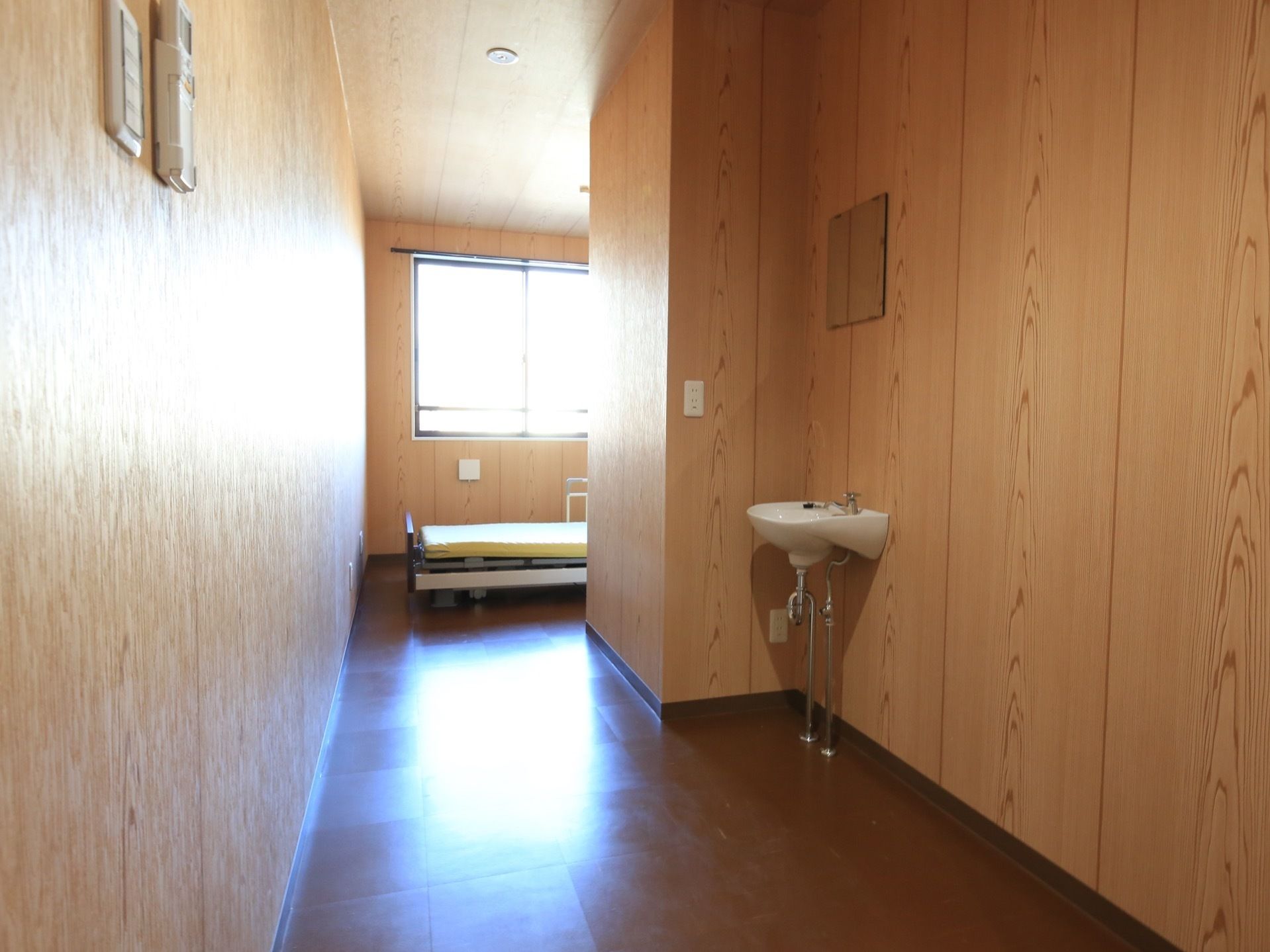 窓から光が差し込む明るい居室。木材を多く使用しており、温もりのある空間となっている。ベッドや洗面台がある。