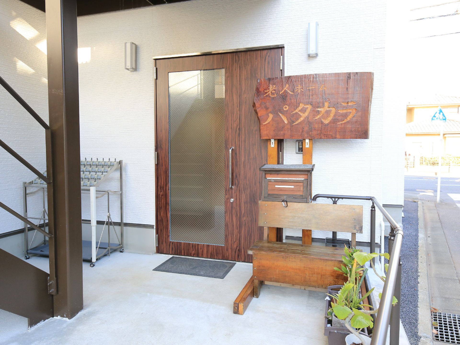 木彫りの看板の下に郵便ポストとベンチが置かれた入り口