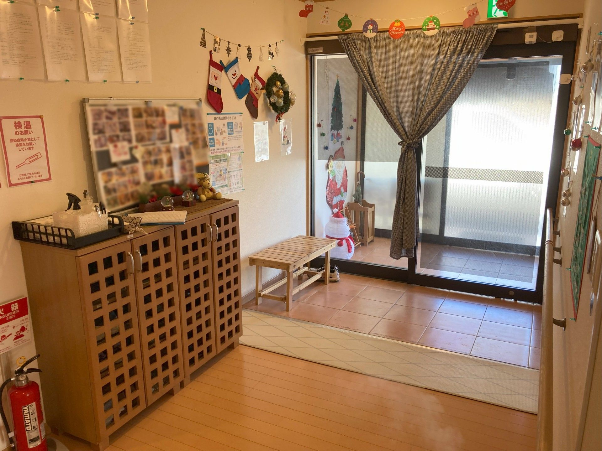 カーディガンを着た高齢女性が車いすに座り、そばには女性スタッフがいて、二人とも微笑んでいる。若い女性スタッフは紺のポロシャツを着ている。