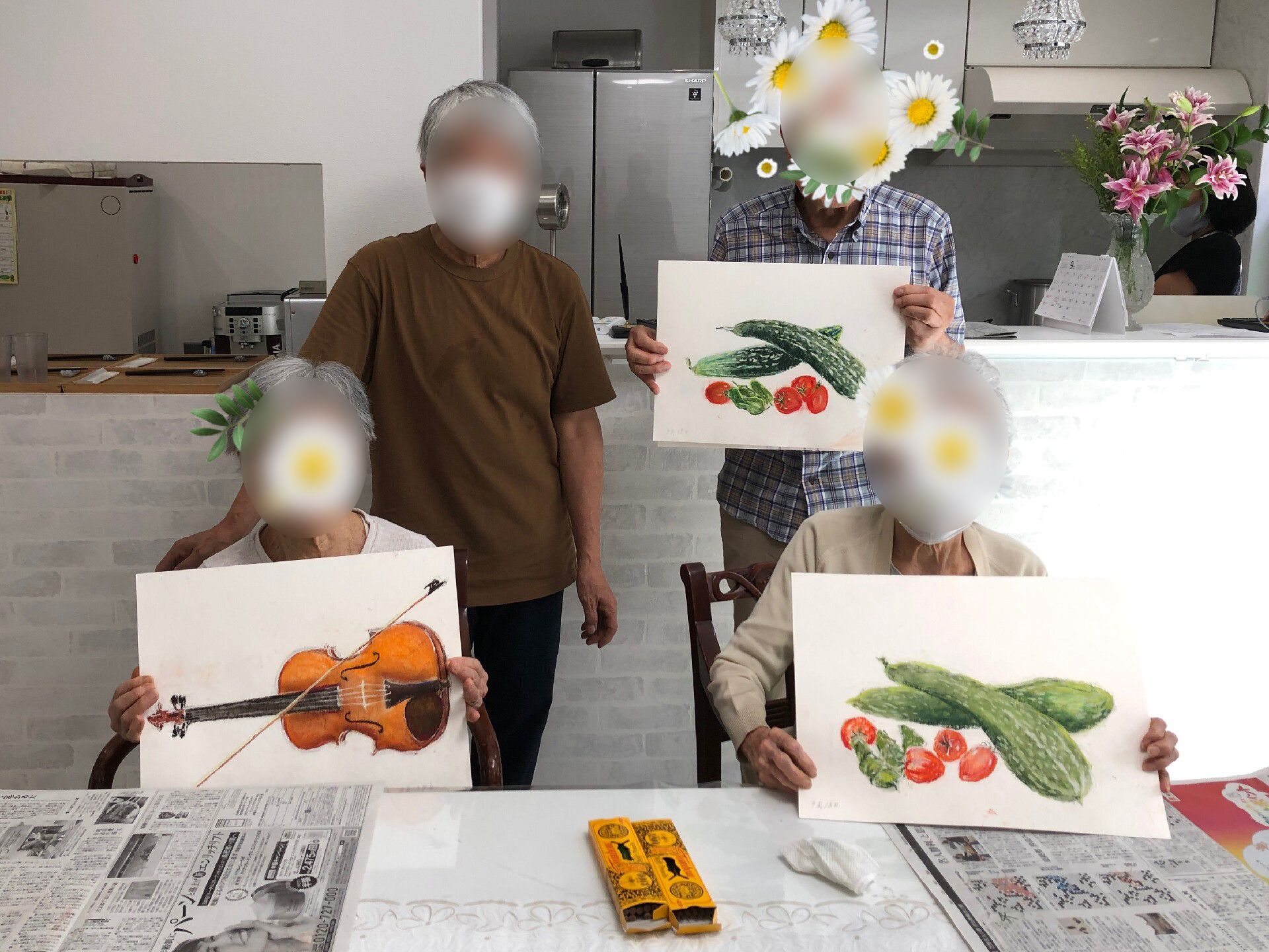 バイオリンやゴーヤとトマトなど、本格的なデッサンが描かれた画用紙を持って講師と共に記念撮影をする男女3人の入居者。