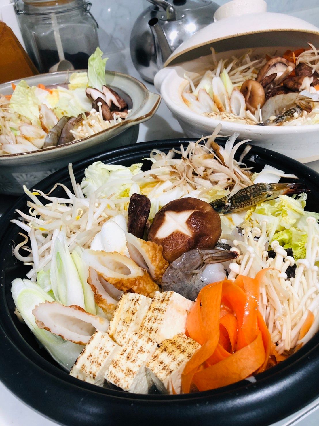 椎茸、人参、焼き豆腐など多数の具材が溢れるように入った大鍋とホットプレートが食卓に用意されている食事