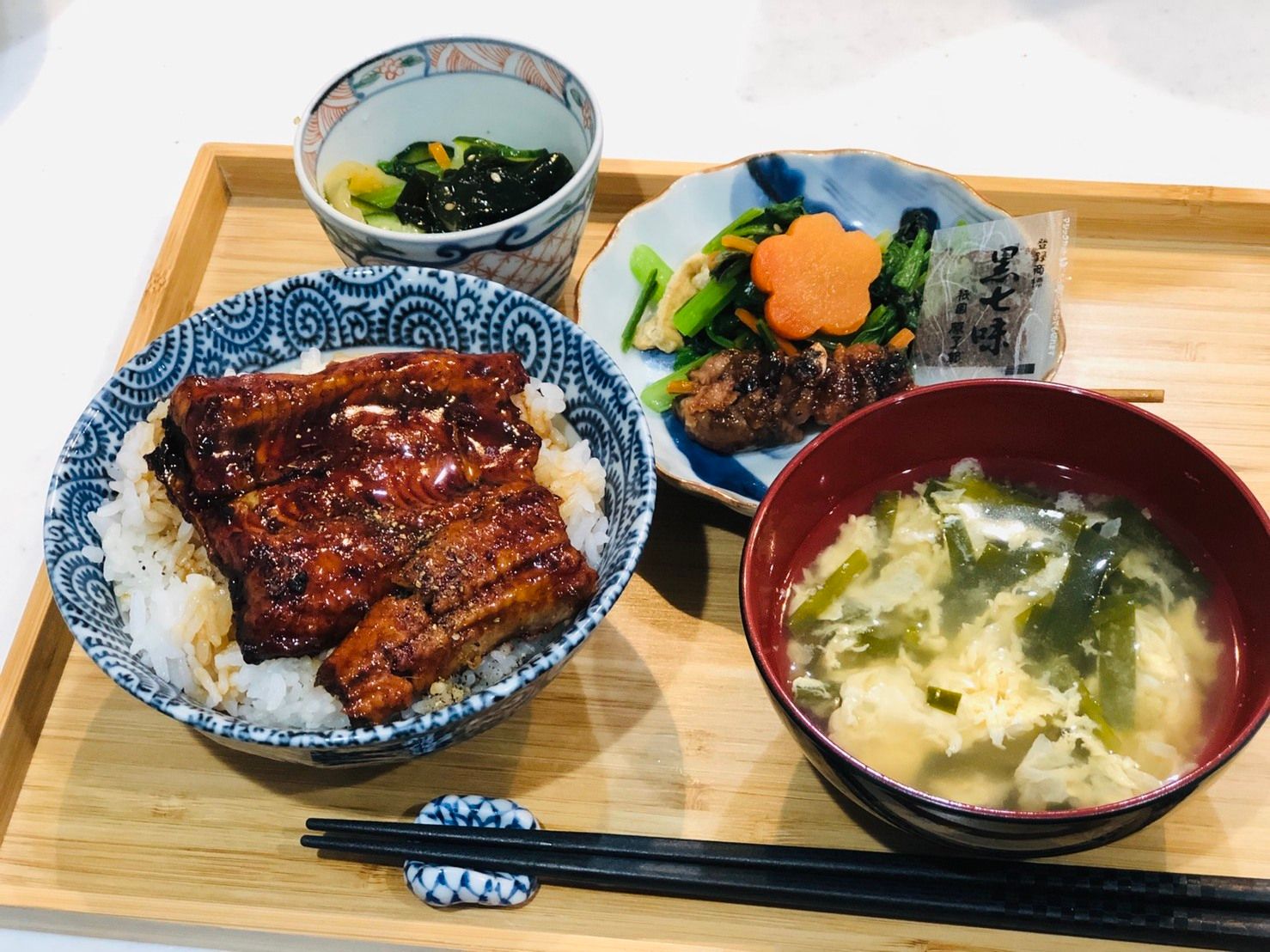 ご飯にうなぎの蒲焼がのっている鰻丼と玉子のお吸い物、野菜料理の小鉢と漬物が用意された食事
