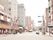 にぎやかな街中の風景。道路を挟んで両サイドにたくさんのビルが建ち並び、飲食店やメガネ屋などがある。