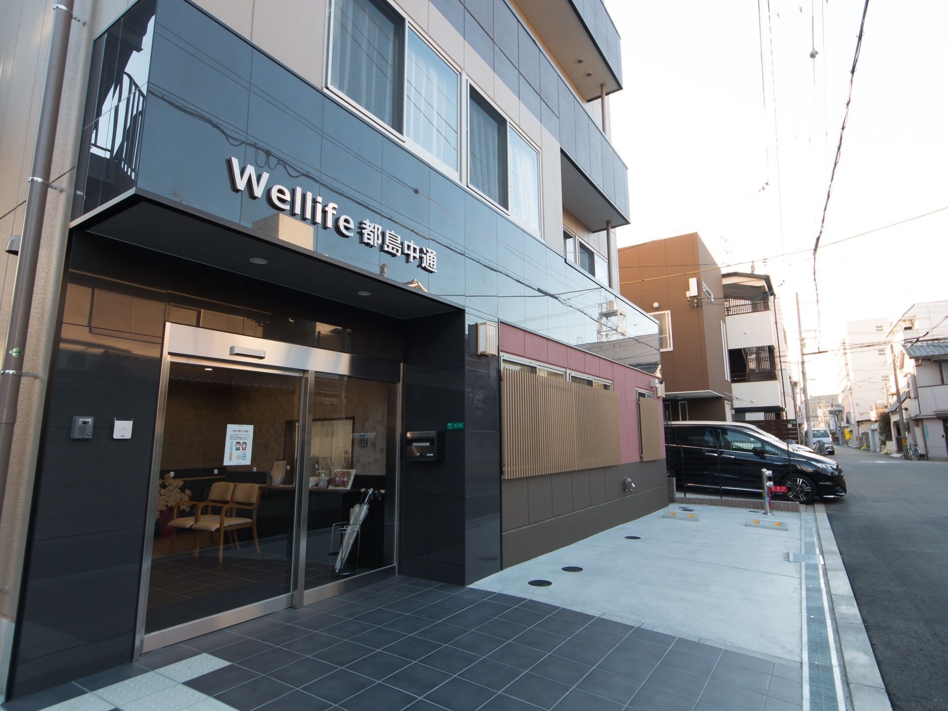 公道に面して、艶のある外壁の施設が建っている。建物の前面は広く平らになっており、コンクリートで舗装された部分に車止めが設置してある。