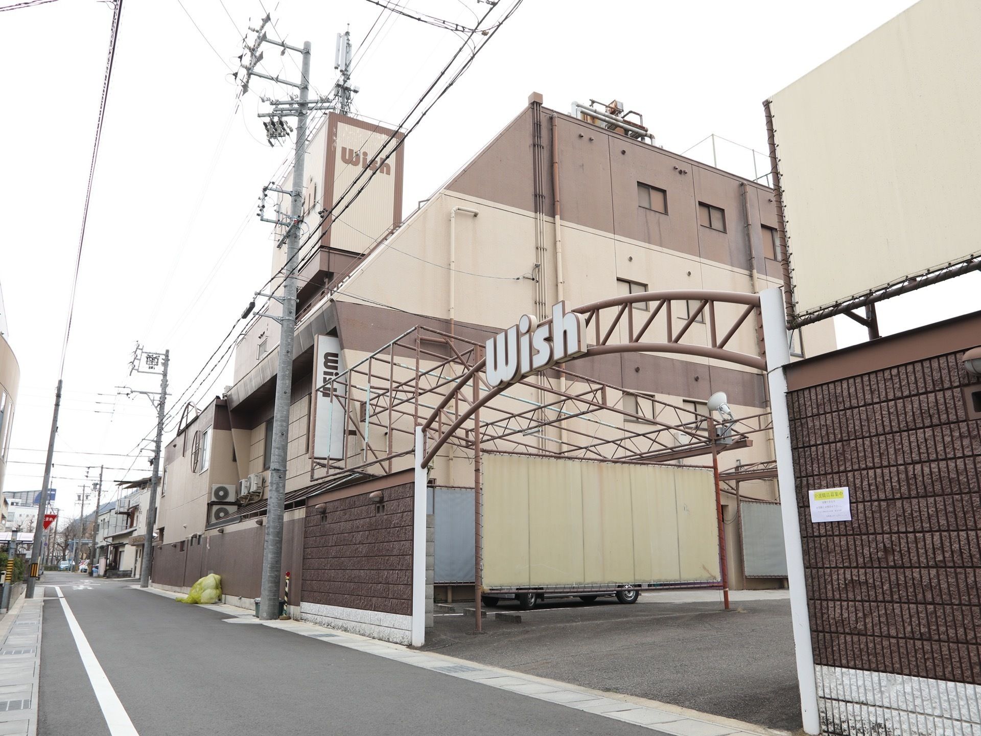 ３階建ての施設建物を対角に見た様子である。外壁はベージュとブラウン系のツートーンカラーで施工されている。